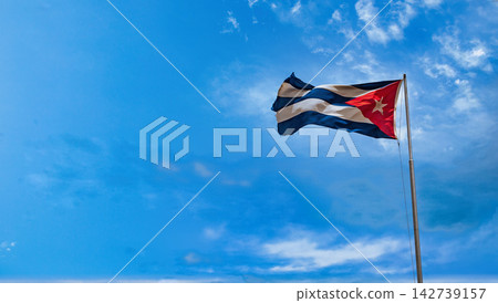 Cuban national flag waving against a bright blue sky with scattered clouds 142739157