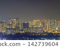 A panoramic nighttime cityscape shows dense high-rise buildings, glowing windows, rooftops, and street lights beneath a hazy dark sky with ample copy space. 142739604
