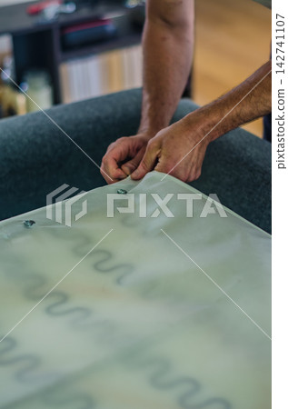 Close-up of a craftsman's hands repairing a sofa. The upholsterer is attaching a protective bottom dust cover fabric over zig-zag sinuous springs. High quality photo Close-up of a craftsman's hands repairing a sofa. The upholsterer is attaching a protective bottom dust cover fabric over zig-zag sinuous springs. High quality photo 142741107