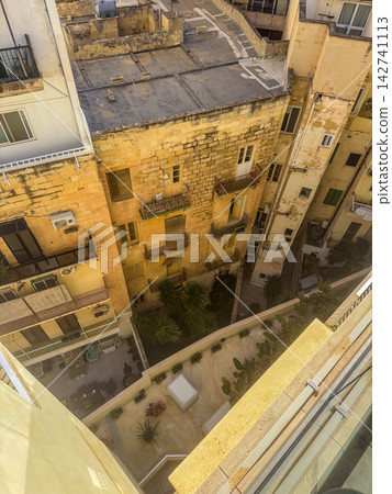 Dramatic overhead view looking down into narrow courtyard between weathered limestone buildings with balconies, rooftops and small garden below. High quality photo Dramatic overhead view looking down into narrow courtyard between weathered limestone buildings with balconies, rooftops and small garden below. High quality photo 142741113