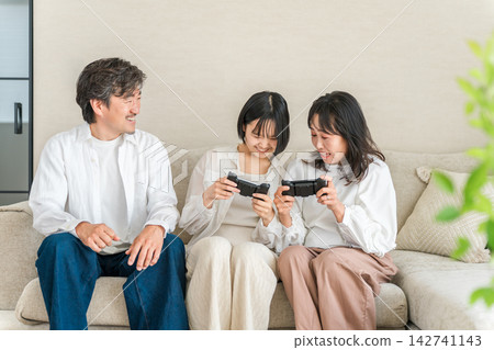 A family of three, smiling and having fun playing video games. Enjoying a relaxing holiday together as a family. A family of three, smiling and having fun playing video games. Enjoying a relaxing holiday together as a family. 142741143