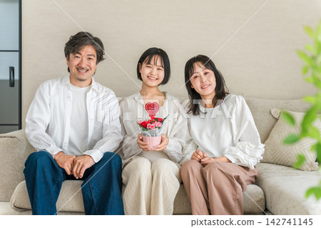 母親節當天,女兒送給父母康乃馨,父母臉上露出笑容。一家人歡慶母親節。 母親節當天,女兒送給父母康乃馨,父母臉上露出笑容。一家人歡慶母親節。 142741145