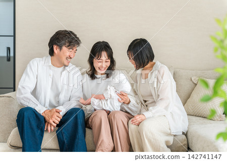 A family of three watches with smiles as the mother holds her baby. The bond between the couple and family that supports child-rearing. A family of three watches with smiles as the mother holds her baby. The bond between the couple and family that supports child-rearing. 142741147