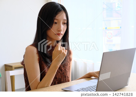 一位年輕女子在辦公桌前使用電腦工作(遠距辦公、商務和工作的圖片)。 一位年輕女子在辦公桌前使用電腦工作(遠距辦公、商務和工作的圖片)。 142741828