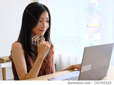 一位年輕女子在辦公桌前使用電腦工作(遠距辦公、商務和工作的圖片)。 一位年輕女子在辦公桌前使用電腦工作(遠距辦公、商務和工作的圖片)。 142741829