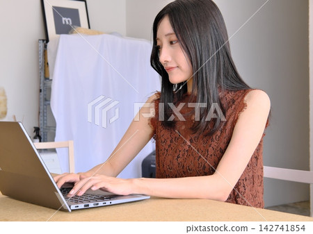 一位年輕女子在辦公桌前使用電腦工作（遠距辦公、商務和工作的圖片）。 142741854
