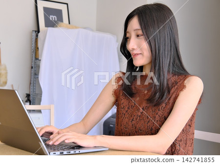 一位年輕女子在辦公桌前使用電腦工作(遠距辦公、商務和工作的圖片)。 一位年輕女子在辦公桌前使用電腦工作(遠距辦公、商務和工作的圖片)。 142741855