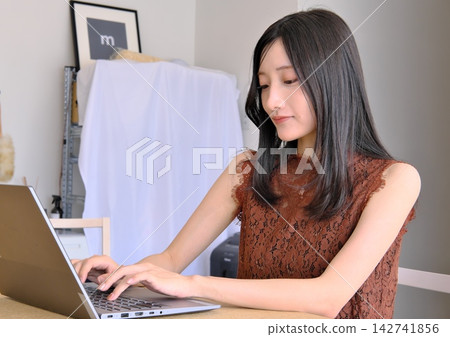 一位年輕女子在辦公桌前使用電腦工作(遠距辦公、商務和工作的圖片)。 一位年輕女子在辦公桌前使用電腦工作(遠距辦公、商務和工作的圖片)。 142741856