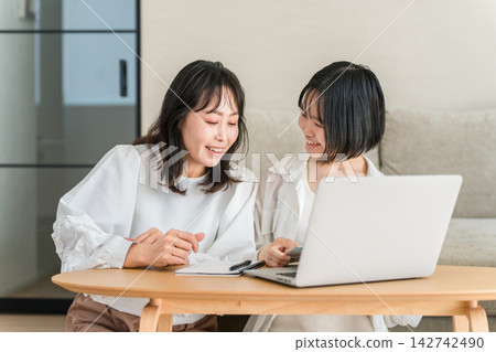 一對母女正在電腦上享受網路購物的樂趣。她們親密地一起瀏覽商品和評論。 一對母女正在電腦上享受網路購物的樂趣。她們親密地一起瀏覽商品和評論。 142742490