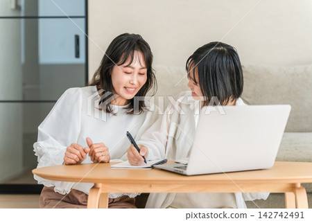 一位母親和女兒一起用電腦和筆記本學習。這種親子關係有助於孩子在家學習。 一位母親和女兒一起用電腦和筆記本學習。這種親子關係有助於孩子在家學習。 142742491