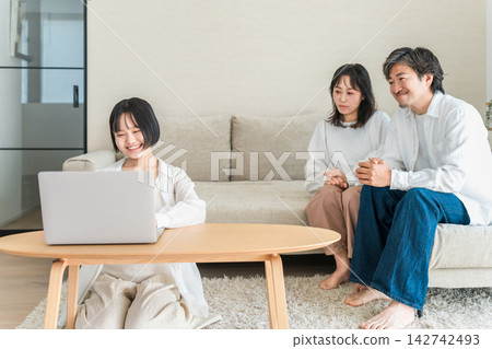 女兒在客廳用電腦學習，父母在一旁看著。這是在家進行的客廳學習。 142742493