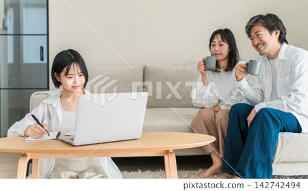 Daughter studies in the living room using a computer and notebook. Parents watch over her homework. Daughter studies in the living room using a computer and notebook. Parents watch over her homework. 142742494