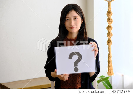 一位年輕女子拿著一張寫著問號的紙(圖片象徵問答、問題、比較) 一位年輕女子拿著一張寫著問號的紙(圖片象徵問答、問題、比較) 142742529