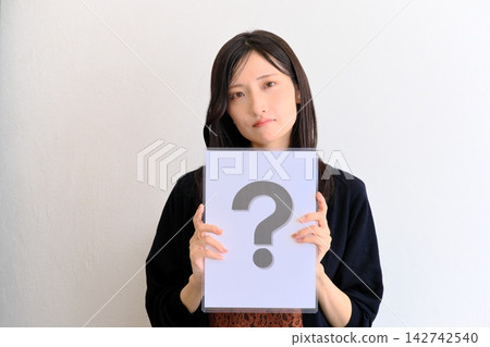一位年輕女子拿著一張寫著問號的紙(圖片象徵問答、問題、比較) 一位年輕女子拿著一張寫著問號的紙(圖片象徵問答、問題、比較) 142742540