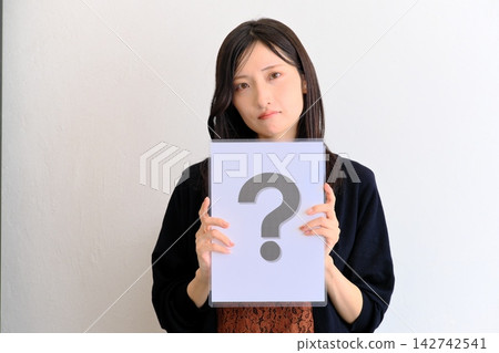 一位年輕女子拿著一張寫著問號的紙(圖片象徵問答、問題、比較) 一位年輕女子拿著一張寫著問號的紙(圖片象徵問答、問題、比較) 142742541