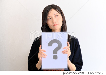 一位年輕女子拿著一張寫著問號的紙(圖片象徵問答、問題、比較) 一位年輕女子拿著一張寫著問號的紙(圖片象徵問答、問題、比較) 142742542