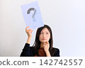 一位年輕女子拿著一張寫著問號的紙（圖片象徵問答、問題、比較） 142742557