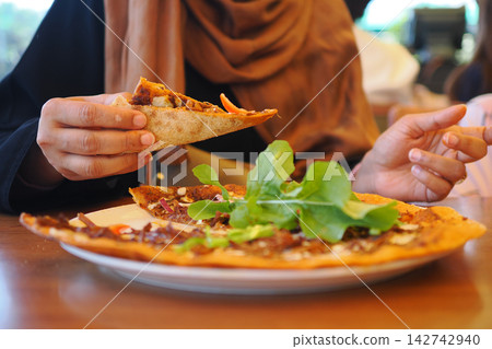 Woman in Headscarf Eating Pizza Slice at Restaurant Table With Fresh Arugula Topping Woman in Headscarf Eating Pizza Slice at Restaurant Table With Fresh Arugula Topping 142742940