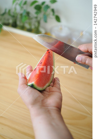 Hands holding a slice of watermelon with a knife above it 142742949
