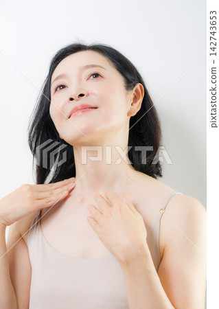 A woman in her 50s cares for her neck and décolleté with both hands; a beauty image of middle-aged women focusing on anti-aging and skincare. A woman in her 50s cares for her neck and décolleté with both hands; a beauty image of middle-aged women focusing on anti-aging and skincare. 142743653