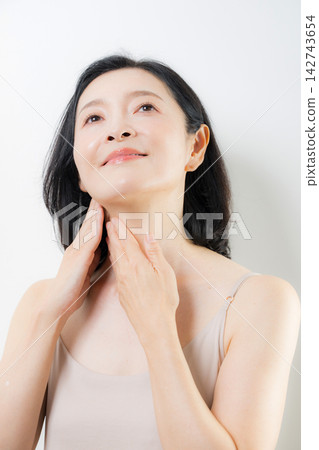A woman in her 50s cares for her neck and décolleté with both hands; a beauty image of middle-aged women focusing on anti-aging and skincare. A woman in her 50s cares for her neck and décolleté with both hands; a beauty image of middle-aged women focusing on anti-aging and skincare. 142743654
