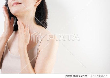 一位五十多歲的女性用雙手仔細照顧頸部和胸前肌膚;一位面無表情的中年美女,專注於抗衰老和護膚。 一位五十多歲的女性用雙手仔細照顧頸部和胸前肌膚;一位面無表情的中年美女,專注於抗衰老和護膚。 142743656