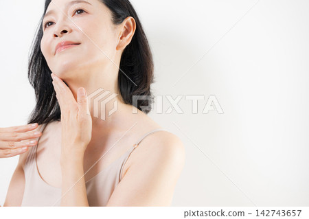 一位 50 多歲的女性用雙手護理頸部和胸前肌膚;展現了中年女性注重抗衰老和護膚的美麗形象。 一位 50 多歲的女性用雙手護理頸部和胸前肌膚;展現了中年女性注重抗衰老和護膚的美麗形象。 142743657