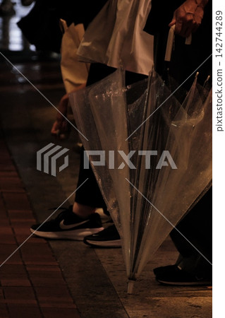 背景圖片為:雨夜中,一個人的雙腳站著,手裡拿著一把收起來的塑膠傘。 背景圖片為:雨夜中,一個人的雙腳站著,手裡拿著一把收起來的塑膠傘。 142744289