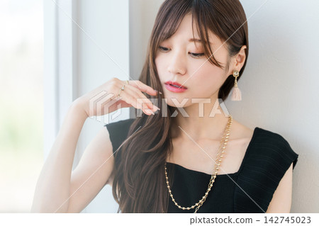 A woman wearing jewelry gazes at her hands. A beauty image highlighting her necklace and earrings. A woman wearing jewelry gazes at her hands. A beauty image highlighting her necklace and earrings. 142745023