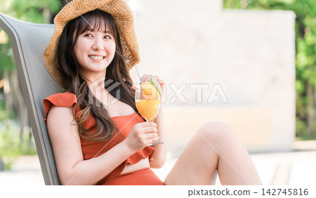 一位身穿泳裝的女子在泳池邊享用熱帶飲品。夏季度假之旅。 一位身穿泳裝的女子在泳池邊享用熱帶飲品。夏季度假之旅。 142745816