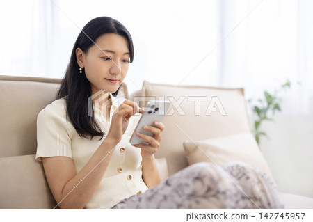 一位年輕的日本女性正在沙發上使用智慧型手機。 142745957