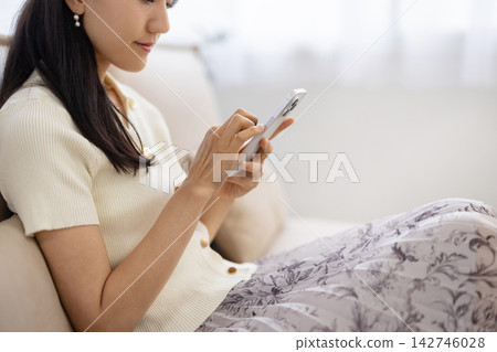 一位年輕的日本女性在沙發上操作智慧型手機，鏡頭特寫她的雙手。 142746028