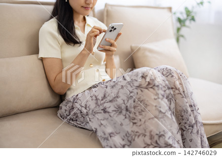 一位年輕的日本女性在沙發上操作智慧型手機，鏡頭特寫她的雙手。 142746029