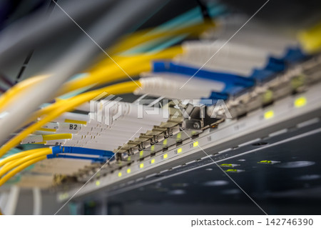Multiple labeled white and yellow fiber optic cables with blue LC connectors inserted into numbered network switch ports with green LED indicators in professional data center rack Multiple labeled white and yellow fiber optic cables with blue LC connectors inserted into numbered network switch ports with green LED indicators in professional data center rack 142746390