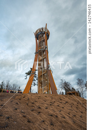 Tall modern wooden observation tower Hamstejn with distinctive curved timber structure and spiral metal staircase surrounded by forest under dramatic cloudy sky, Czech Republic Tall modern wooden observation tower Hamstejn with distinctive curved timber structure and spiral metal staircase surrounded by forest under dramatic cloudy sky, Czech Republic 142746435