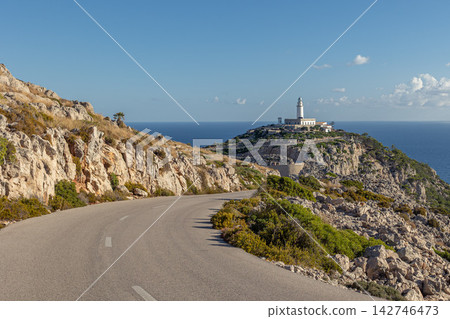 Winding road leading to Far de Formentor lighthouse on Mallorca northern tip, surrounded by rocky cliffs, Mediterranean Sea views, and bright clear sky Winding road leading to Far de Formentor lighthouse on Mallorca northern tip, surrounded by rocky cliffs, Mediterranean Sea views, and bright clear sky 142746473