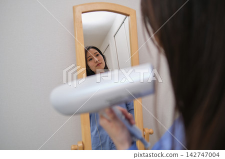 晨間日常:一位女士一邊照鏡子一邊整理頭髮。 晨間日常:一位女士一邊照鏡子一邊整理頭髮。 142747004