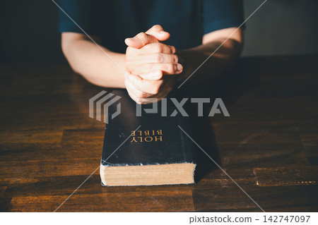 Close-up of clasped hands above a closed Holy Bible on a wooden table, symbolizing prayer, Christian faith, devotion, worship, scripture, spiritual reflection, hope, trust, gratitude, and peace. Close-up of clasped hands above a closed Holy Bible on a wooden table, symbolizing prayer, Christian faith, devotion, worship, scripture, spiritual reflection, hope, trust, gratitude, and peace. 142747097