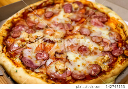 Freshly baked delicious pizza with various sausages, chicken meat, and melted cheese in a cardboard delivery box. Fast food and italian cuisine concept Freshly baked delicious pizza with various sausages, chicken meat, and melted cheese in a cardboard delivery box. Fast food and italian cuisine concept 142747133
