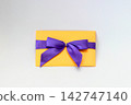 Yellow envelope tied with a purple satin ribbon bow, isolated on a white background. Gift, invitation, and celebration concept 142747140