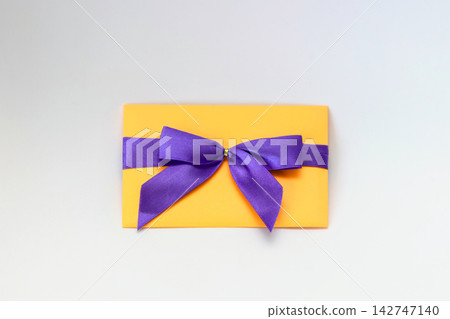 Yellow envelope tied with a purple satin ribbon bow, isolated on a white background. Gift, invitation, and celebration concept Yellow envelope tied with a purple satin ribbon bow, isolated on a white background. Gift, invitation, and celebration concept 142747140