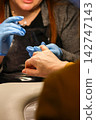 Nail technician wearing blue gloves performing a manicure procedure on a client's hand in a salon. Beauty, care, and hygiene concept 142747143