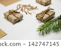 Wrapped small gift boxes with twine rope, craft paper envelopes, and a pine branch on a white background. Christmas flat lay 142747145