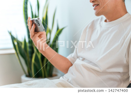 一個男人躺在床上,看著他的智慧型手機。這是睡前在家放鬆的場景。 一個男人躺在床上,看著他的智慧型手機。這是睡前在家放鬆的場景。 142747400