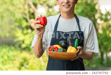一位男子麵帶微笑，手持新鮮採摘的夏季蔬菜。這幅畫面象徵著農民、產地直送以及家鄉稅收捐贈的概念。 142747742
