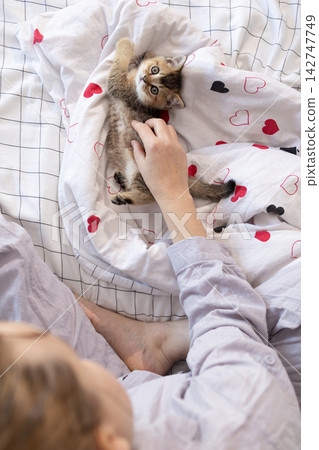 Woman petting a kitten on a bed at home in an overhead view 142747749