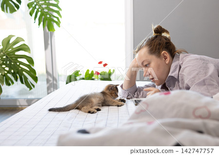 Woman resting face to face with a kitten on bed at home in the morning Woman resting face to face with a kitten on bed at home in the morning 142747757