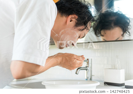 一名男子在浴室洗手台用清水沖掉臉上的泡沫。這是男士晨間洗臉和護膚的日常流程。 一名男子在浴室洗手台用清水沖掉臉上的泡沫。這是男士晨間洗臉和護膚的日常流程。 142748425