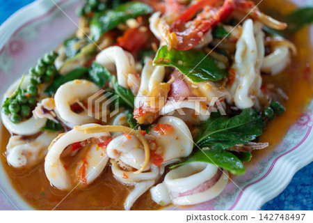 Spicy Thai stir fried squid fresh basil chili garlic peppercorns savory sauce served as authentic seafood cuisine traditional Thai meal Spicy Thai stir fried squid fresh basil chili garlic peppercorns savory sauce served as authentic seafood cuisine traditional Thai meal 142748497