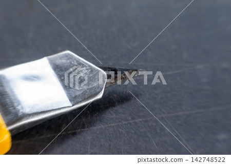Close up of utility knife exposed metal blade resting dark scratched surface representing cutting tools repair maintenance craft workshop equipment Close up of utility knife exposed metal blade resting dark scratched surface representing cutting tools repair maintenance craft workshop equipment 142748522